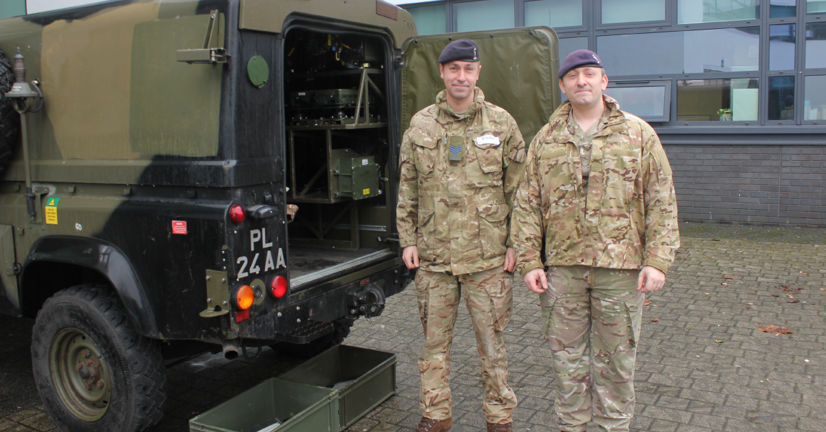 Army officers stand beside Land Rover Defender during visit to college.