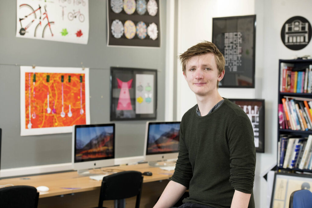 student in front of artwork on walls and computers