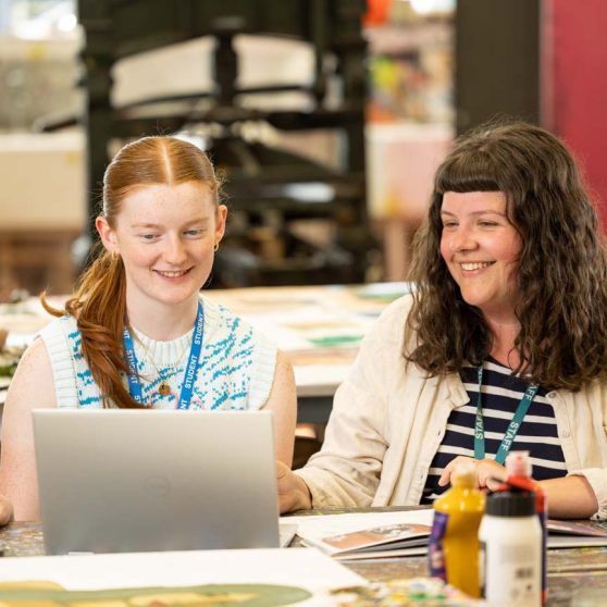 Student on a laptop in an art classroom sitting next to a tutor