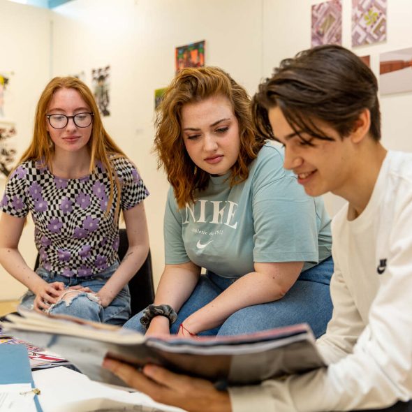 three students in a library reading a book